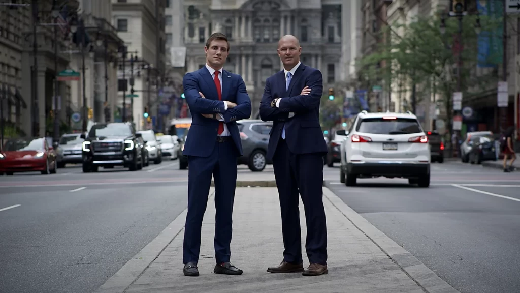 Why Refer to Us — Leadership on Broad Street, Philadelphia - McMenamin & Wing - Workers' Comp Lawyers Two attorneys on Broad Street with Philadelphia City Hall behind them; leadership of a Pennsylvania workers’ compensation firm.
